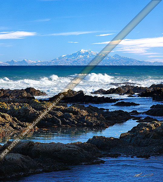 Photo of Wild Wellington south coast. Waves rolling in from Cook Strait with snow covered Inland Kaikoura Mountain Ranges beyond. Rockpools in foreground, Wellington, Wellington City, Wellington Region, New Zealand (NZ)