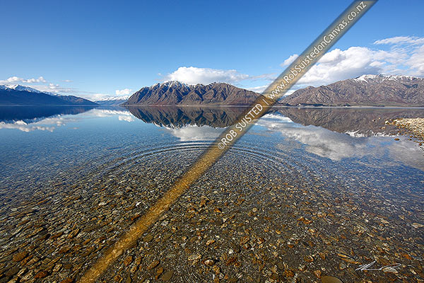 Photo of Lake Hawea on a perfect calm spring/winter day reflecting the surrounding snowy ranges. Mirror calm lake surface with ripples and rings, Lake Hawea, Queenstown Lakes, Otago Region, New Zealand (NZ)