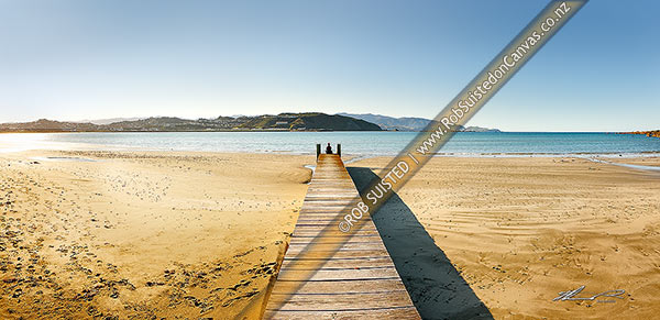 Photo of Lyall Bay Beach with person sitting or meditating on end of wooden boardwalk on a fine spring morning, with Wellington Airport beyond. Panorama, Lyall Bay, Wellington City, Wellington Region, New Zealand (NZ)