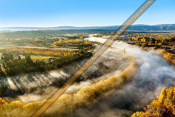 Photo of Clutha River Mata-Au with morning mist and golden autumn colours. Aerial view over river, stonefruit orchards and old gold workings, Alexandra, Central Otago, Otago Region, New Zealand (NZ)