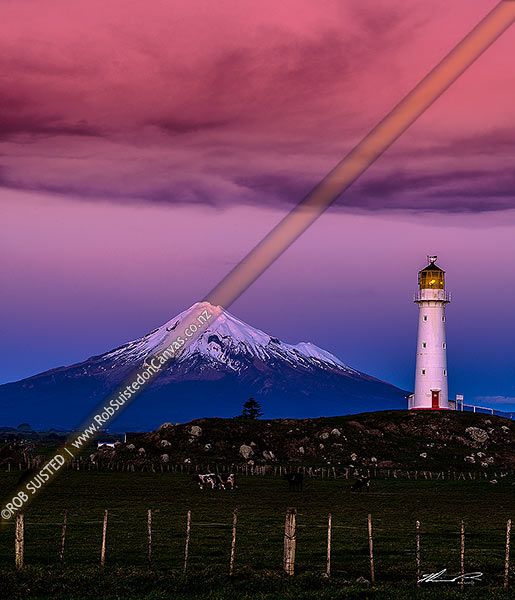 Photo of Cape Egmont and lighthouse, with a snow cloaked Mt Taranaki behind. After dusk, Cape Egmont, South Taranaki, Taranaki Region, New Zealand (NZ)