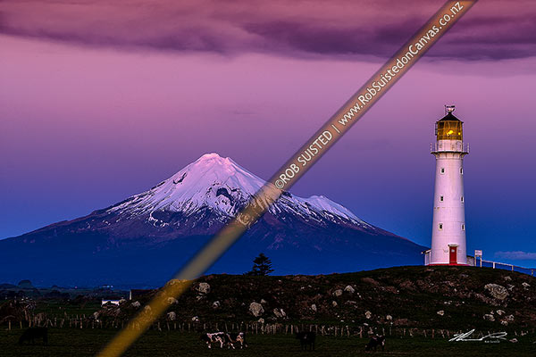 Photo of Cape Egmont and lighthouse, with a snow cloaked Mt Taranaki behind. After dusk, Cape Egmont, South Taranaki, Taranaki Region, New Zealand (NZ)