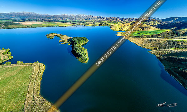 Photo of Lake Opuha and island, a man made lake for irrigation and power generation, with Sherwood Range beyond lush green farmland around Ashwick Flat. Aerial panorama, Fairlie, MacKenzie, Canterbury Region, New Zealand (NZ)