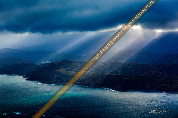 Photo of Wellington Harbour entrance with sun ray breaking through heavy cloud over Gollans Stream and East Harbour Regional Park. Moody aerial view, Wellington Harbour, Wellington City, Wellington Region, New Zealand (NZ)